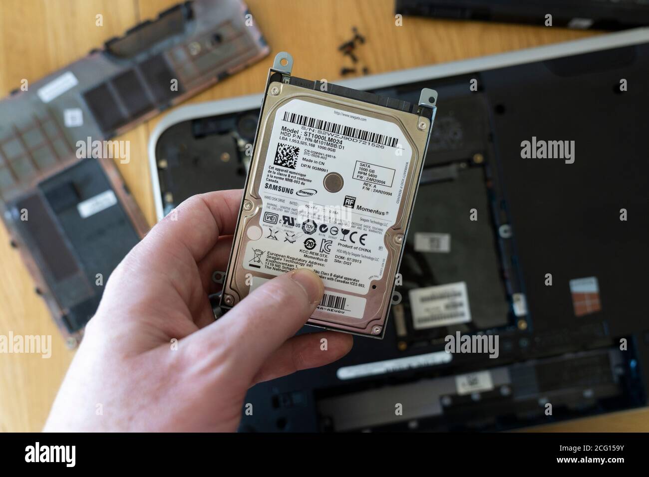 Mano dell'uomo che tiene un'unità disco rigido (HDD) Seagate da 2.5' rimossa da un computer portatile. Tema: Memorizzazione dei dati, riparazione del computer, sostituzione della vecchia tecnologia, memoria Foto Stock