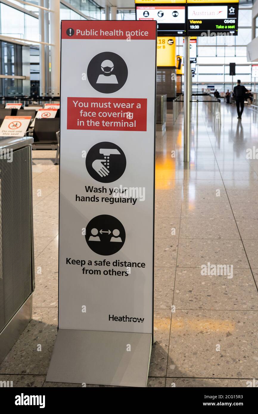 Avviso di salute pubblica che fornisce istruzioni ai passeggeri dell'aeroporto di Heathrow per indossare una maschera, lavarsi le mani e mantenere una distanza di sicurezza per la pandemia di Covid-19 Foto Stock