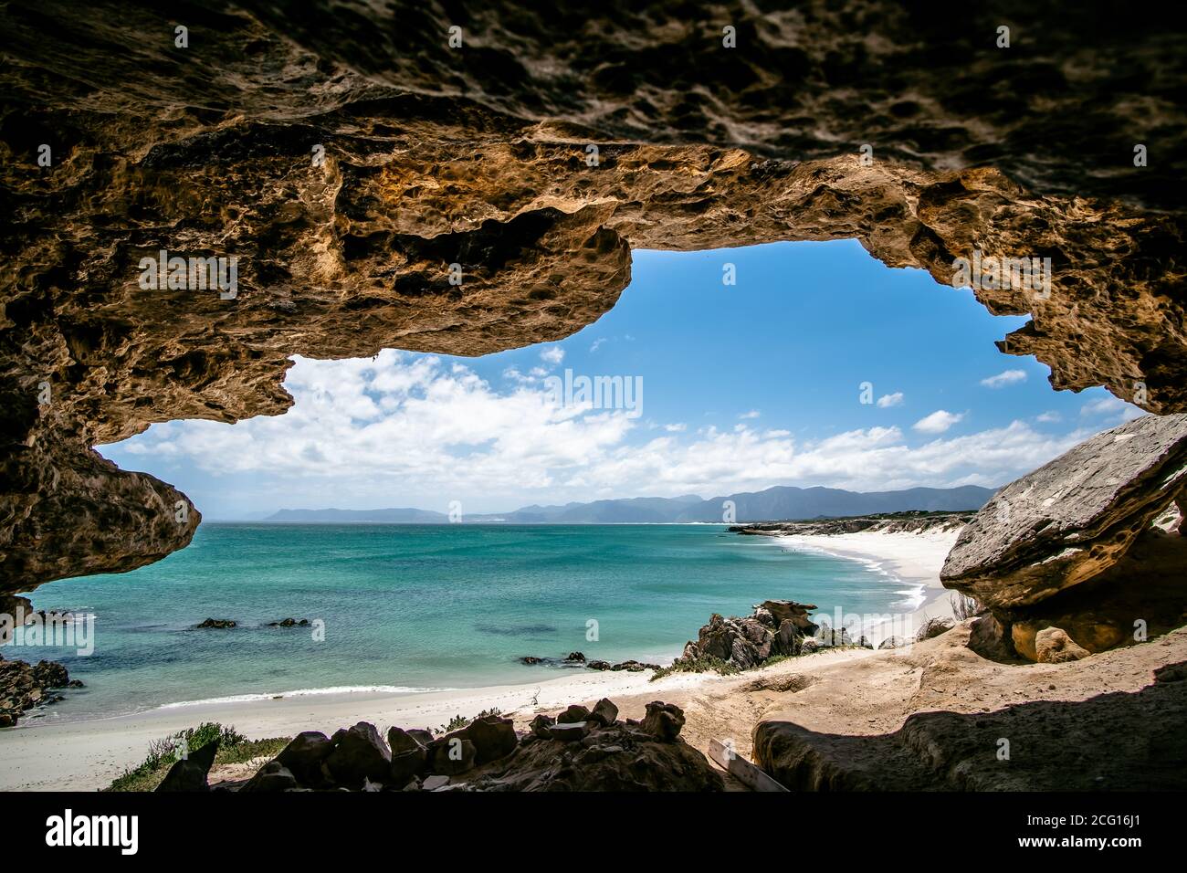 Immacolato tratto di spiaggia bianca appartata con allure acque blu, sparato dalla grande grotta, bella giornata di sole Foto Stock
