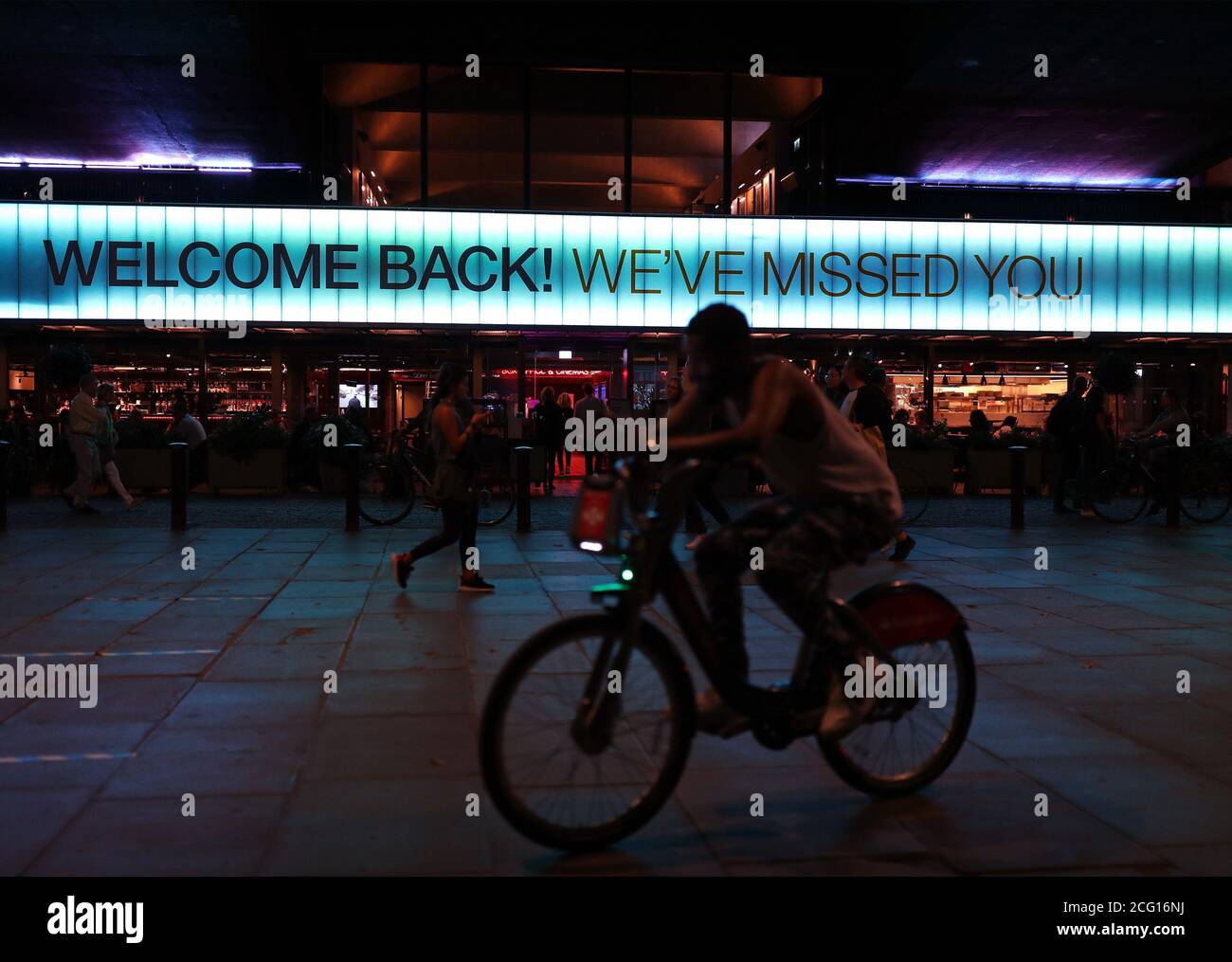 Un ciclista passa davanti a un cartello che dice 'Bentornato! Ti abbiamo perso" esposto sopra la parte anteriore del cinema BFI Southbank di Londra. Foto Stock
