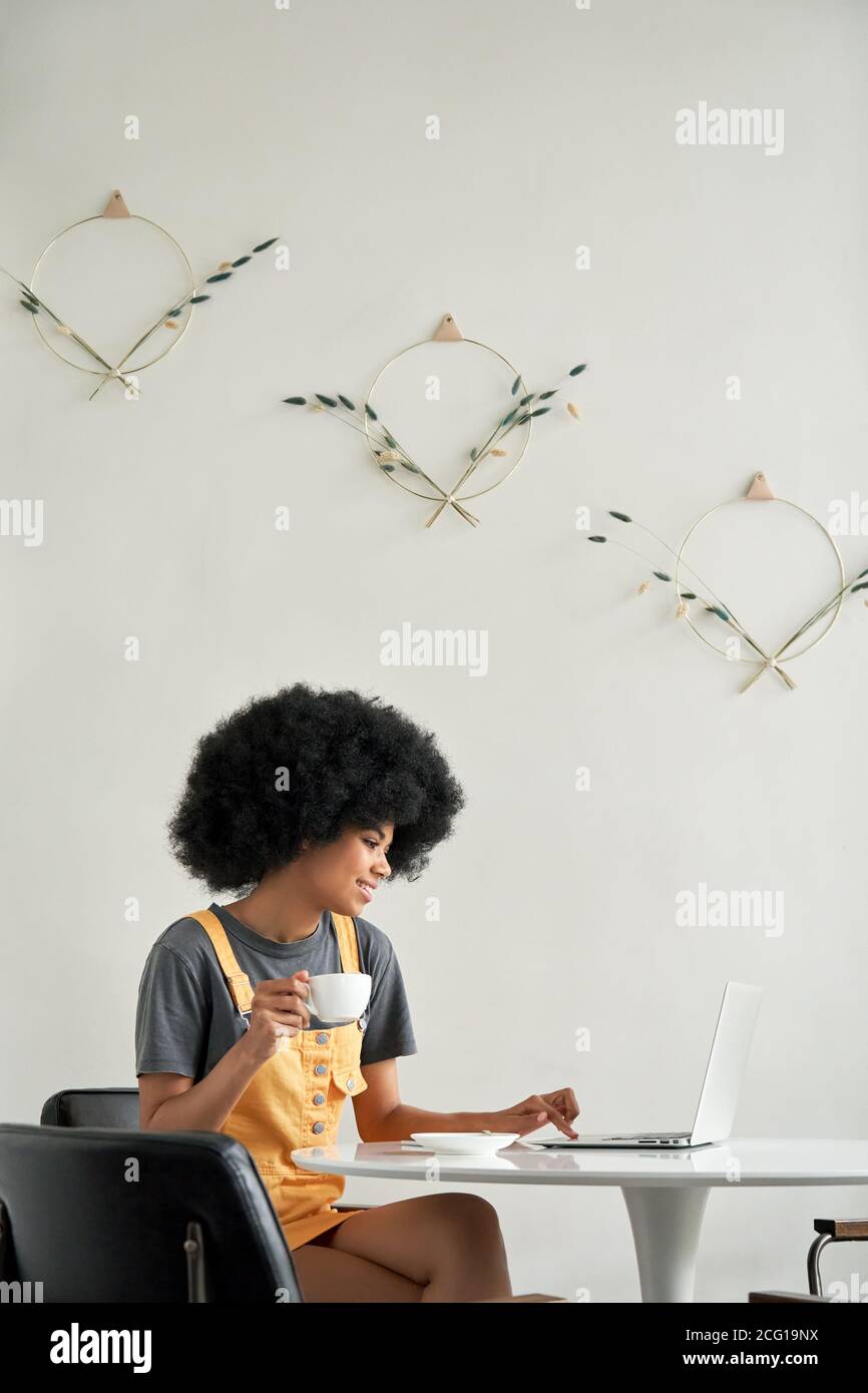 Happy African lady studentessa utilizzando il computer portatile sedersi al tavolo in caffè bere caffè. Foto Stock