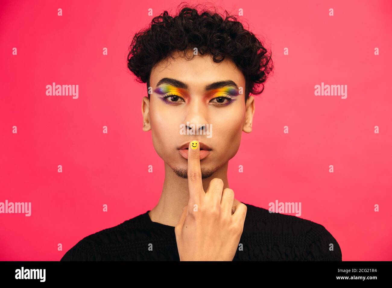 L'uomo gay che indossa l'ombra colorata dell'occhio iridato e l'unghia sorridente del viso mettendo il dito nelle labbra, gesturando di essere abbastanza. Transgender uomini gesturing si Foto Stock