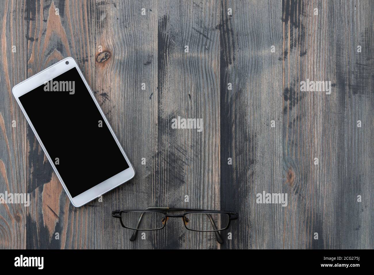 Smartphone mobile con schermo nero e vecchi occhiali su sfondo in legno vintage. Disposizione piatta, spazio di copia Foto Stock