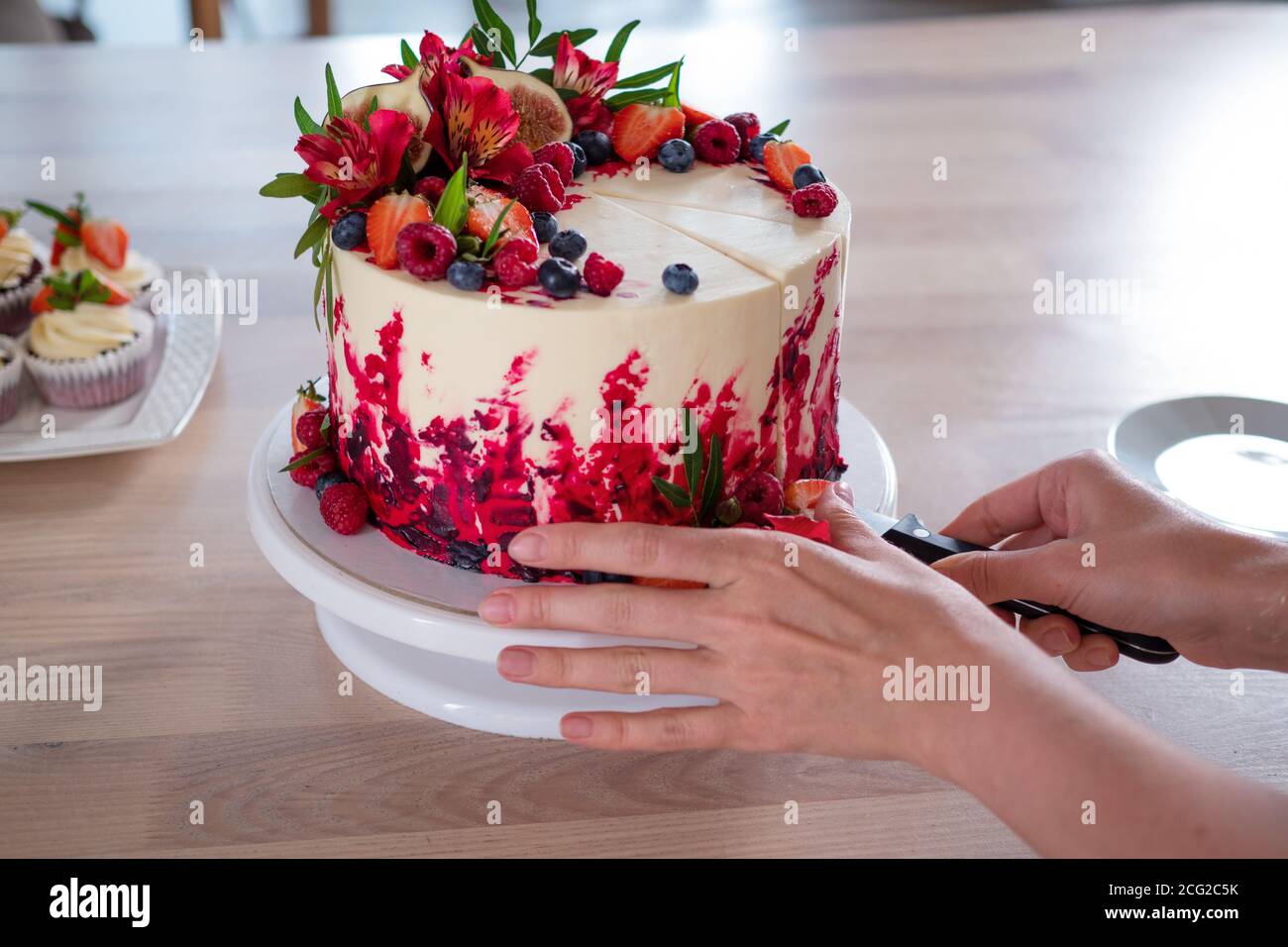 Grande bella torta di velluto rosso, con fiori e bacche in cima. Tagliare una porzione, le mani da vicino delle donne. Foto Stock