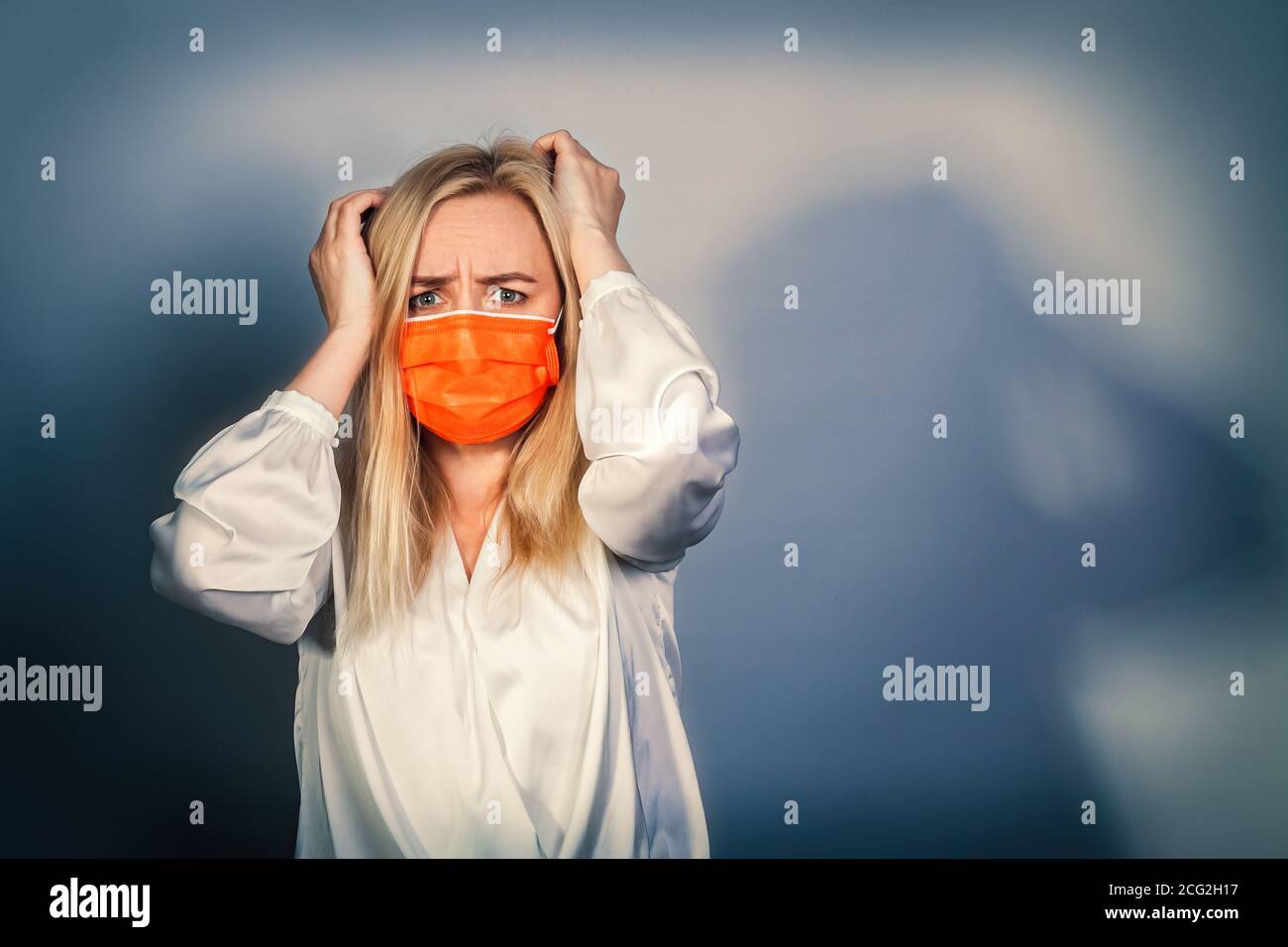 Donna con una faccia terrorizzata in una maschera medica arancione tiene la testa. Foto Stock