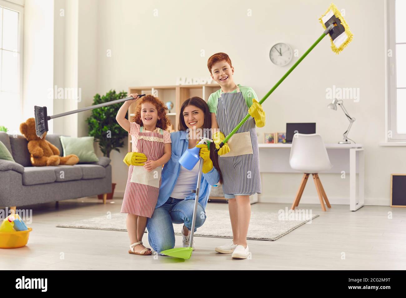 Mamma e bambini felici con le spazzolette da pavimento e la padella sorridente e guardare la fotocamera dopo un grande clear-out Foto Stock