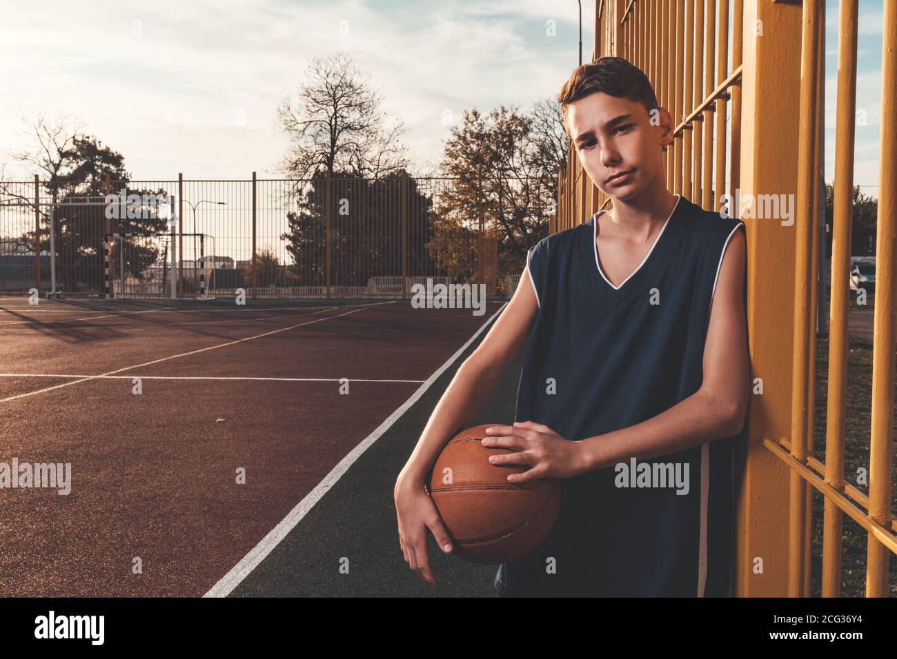 Sport e basket. Un giovane adolescente in una tuta nera posa con un basket,  in piedi alla recinzione. Spazio di copia Foto stock - Alamy
