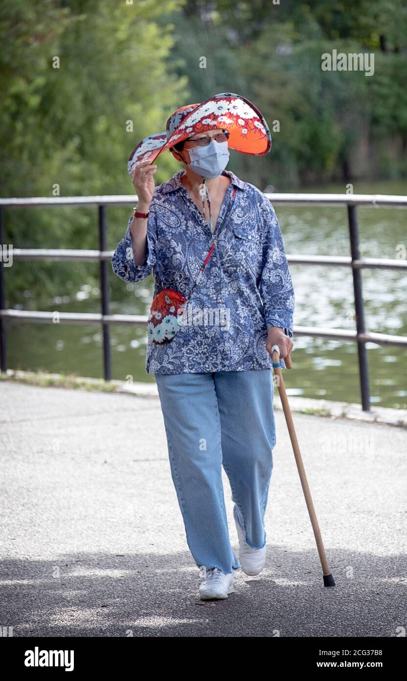 Una donna elegante nei suoi anni settanta va per una camminata di esercitazione che indossa una maschera chirurgica & cappello di corrispondenza & borsa. In un parco a Flushing, Queens, New York. Foto Stock