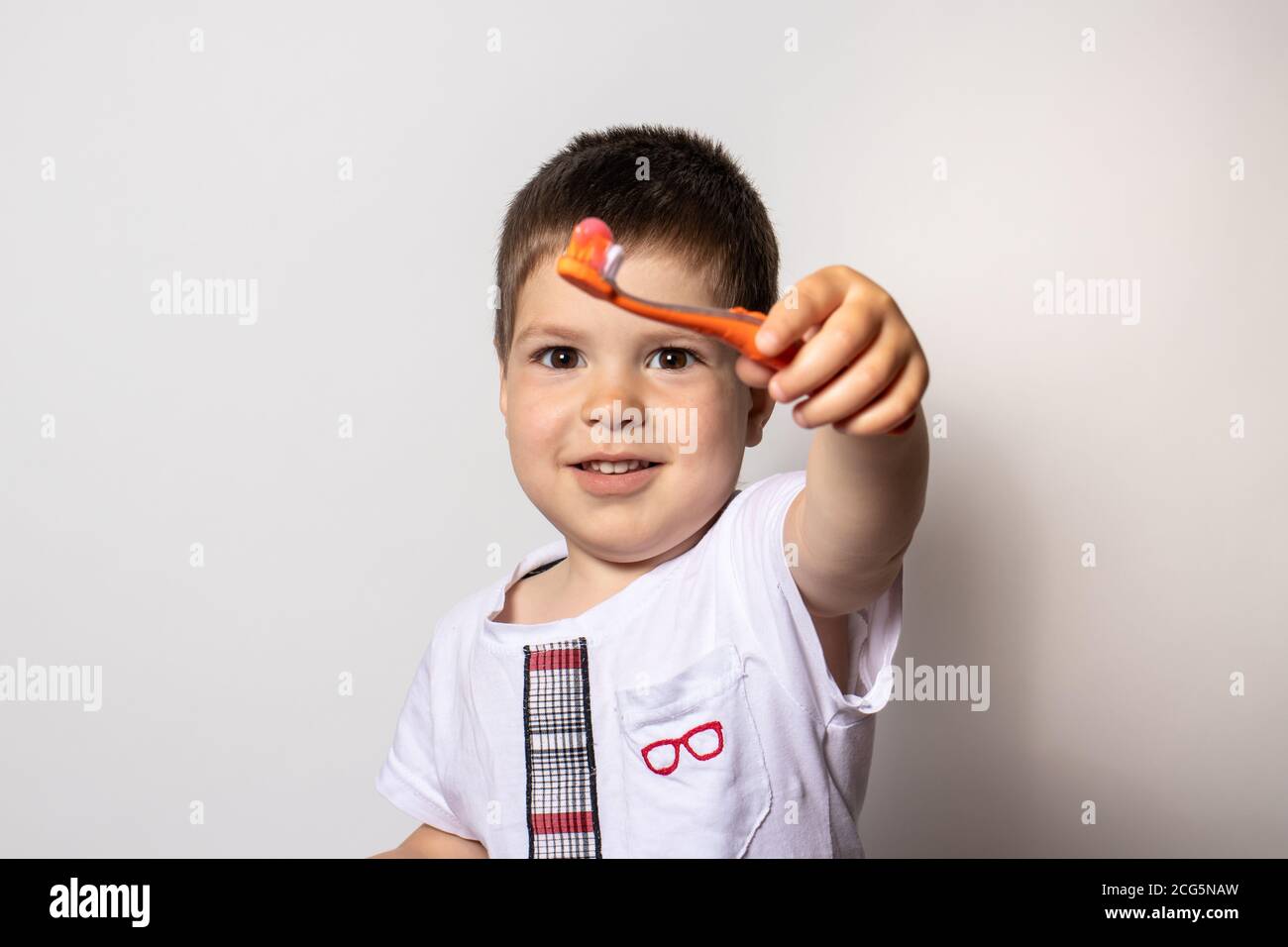 Un ragazzo carino di 3 anni mostra uno spazzolino da denti con dentifricio rosa per bambini su sfondo bianco. Spazzolando i denti dei bambini Foto Stock