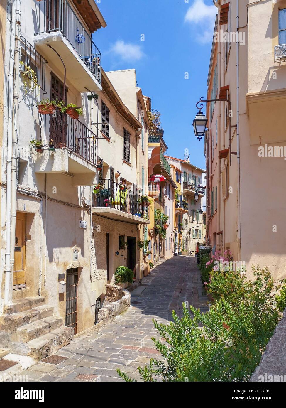 Vuota stradina collinare con pavimento in pietra lucido e vecchi edifici a tre piani con balconi decorati con piante verdi in vasi di fiori a Nizza. Foto Stock