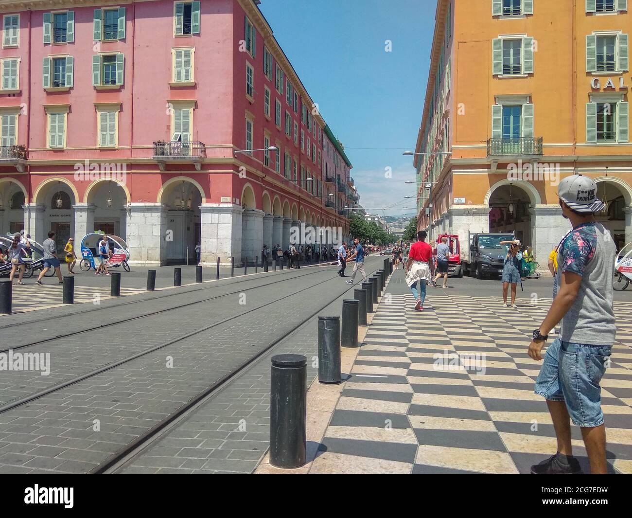 Persone che scattano foto e camminano vicino a edifici in ocra rossa con tram tra loro in Place Massena, nel centro di Nizza, Francia. Foto Stock
