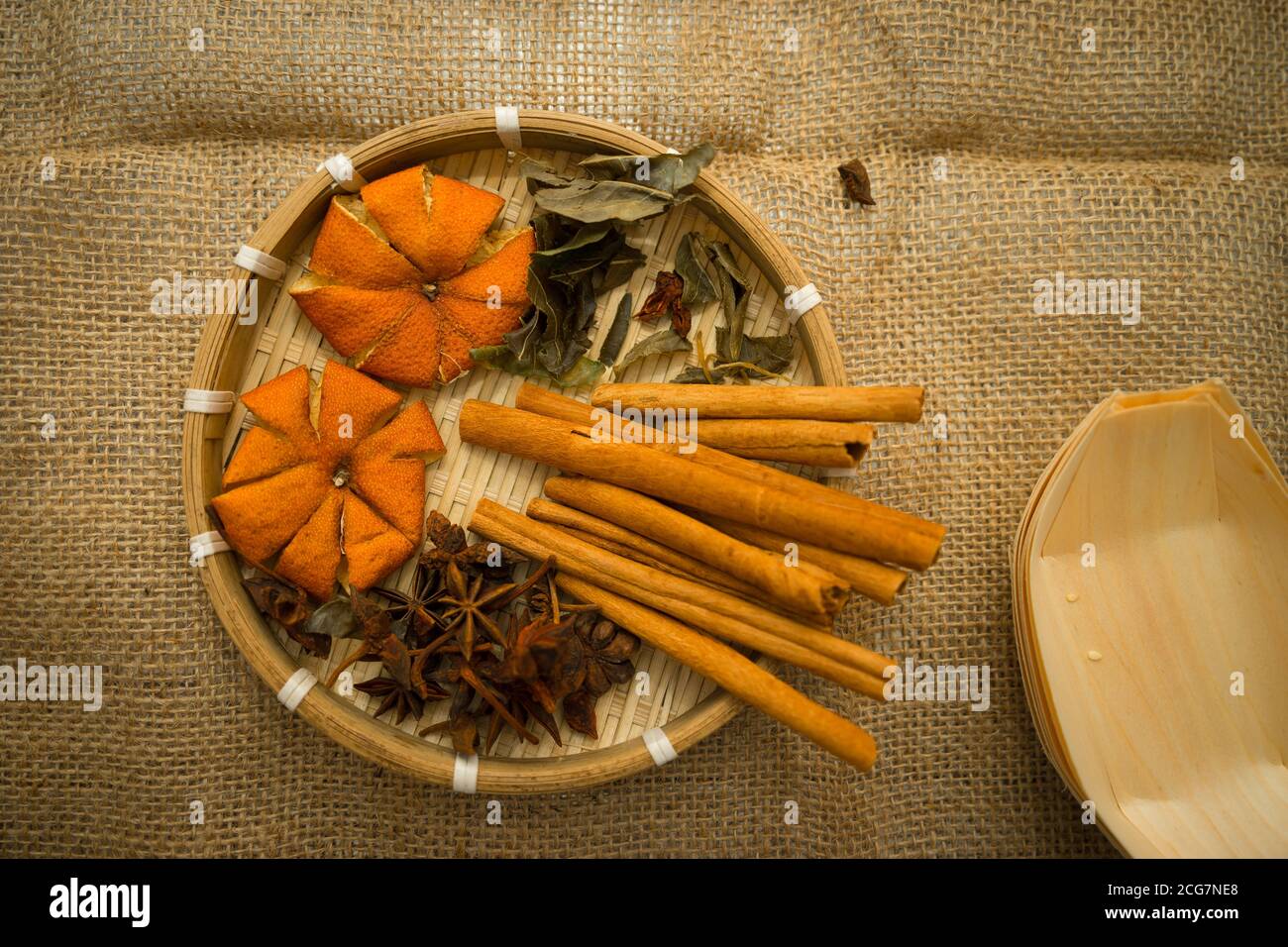 Vista dall'alto della buccia di mandarino essiccata, dei bastoncini di  cannella e dell'anice stellato nel vassoio di legno di bambù in tessuto  sullo sfondo del burlap - concetto di erbe e spezie