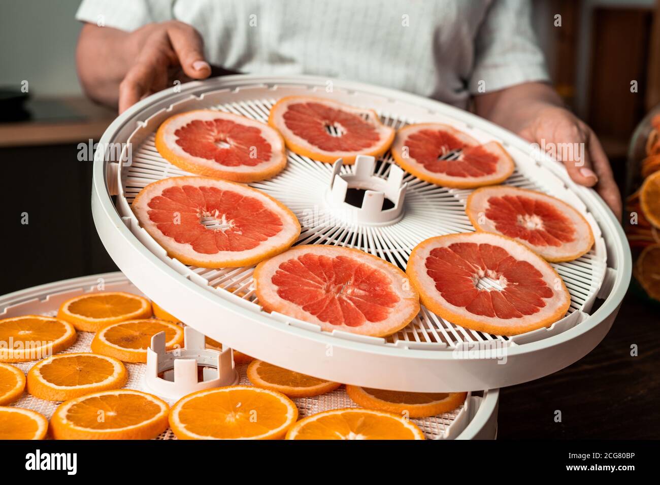 Primo piano di una donna irriconoscibile che monta vassoi di plastica disidratatore con fresco frutta in cucina Foto Stock