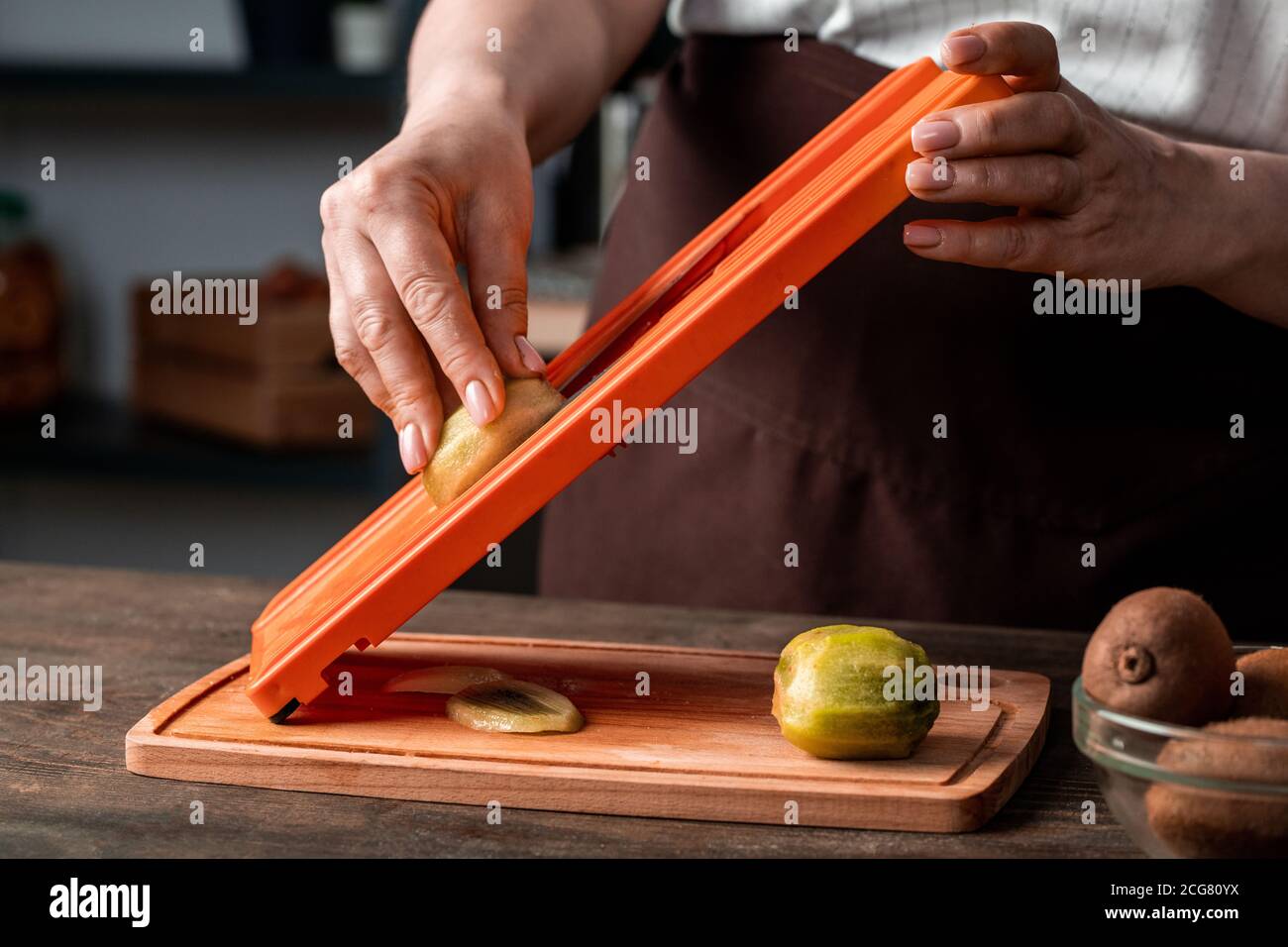 Primo piano di donna irriconoscibile che taglia kiwi su affettatrice sopra legno asse in cucina Foto Stock