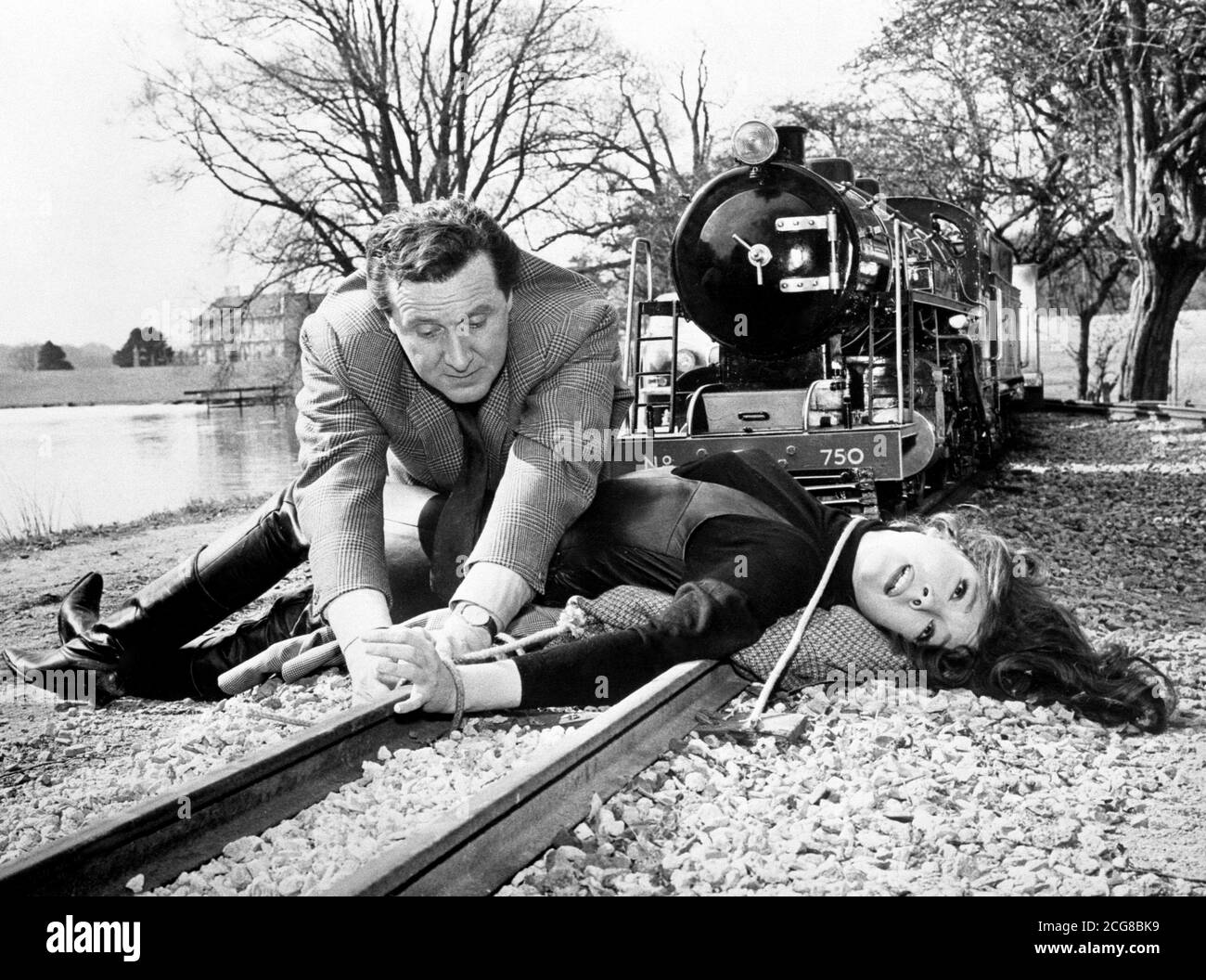 L'agente speciale John Steed (Patrick Macnee) è lì appena in tempo per salvare il bel collo di Emma Peel (Diana Rigg) in una scena in fase di ripresa per la nuova serie di 'The Avengers'. La posizione era la ferrovia in miniatura nella tenuta di Lord Gretton's Stapleford Park. Foto Stock