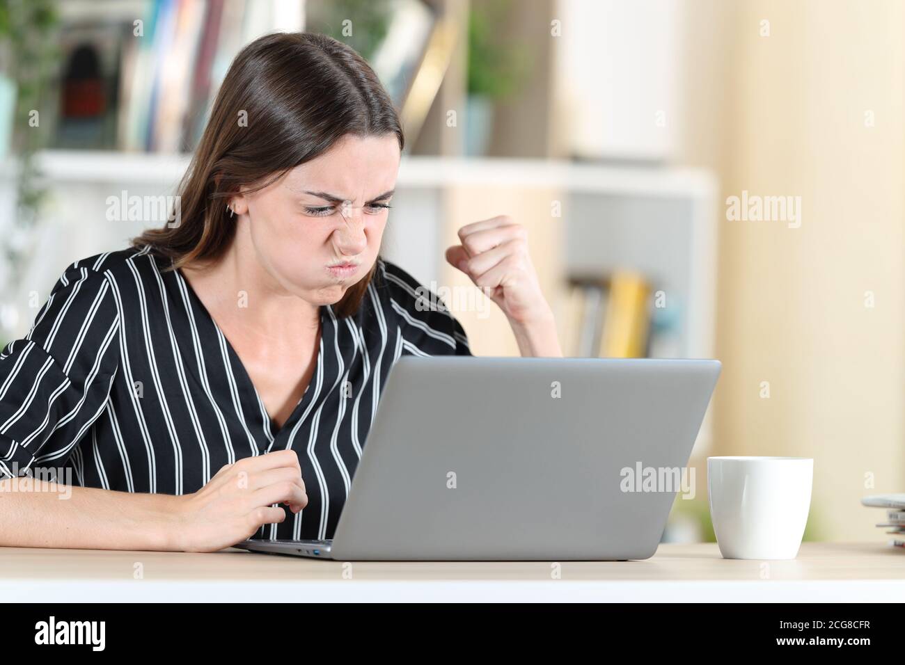 Donna arrabbiata che controlla il laptop seduto in una scrivania a casa Foto Stock