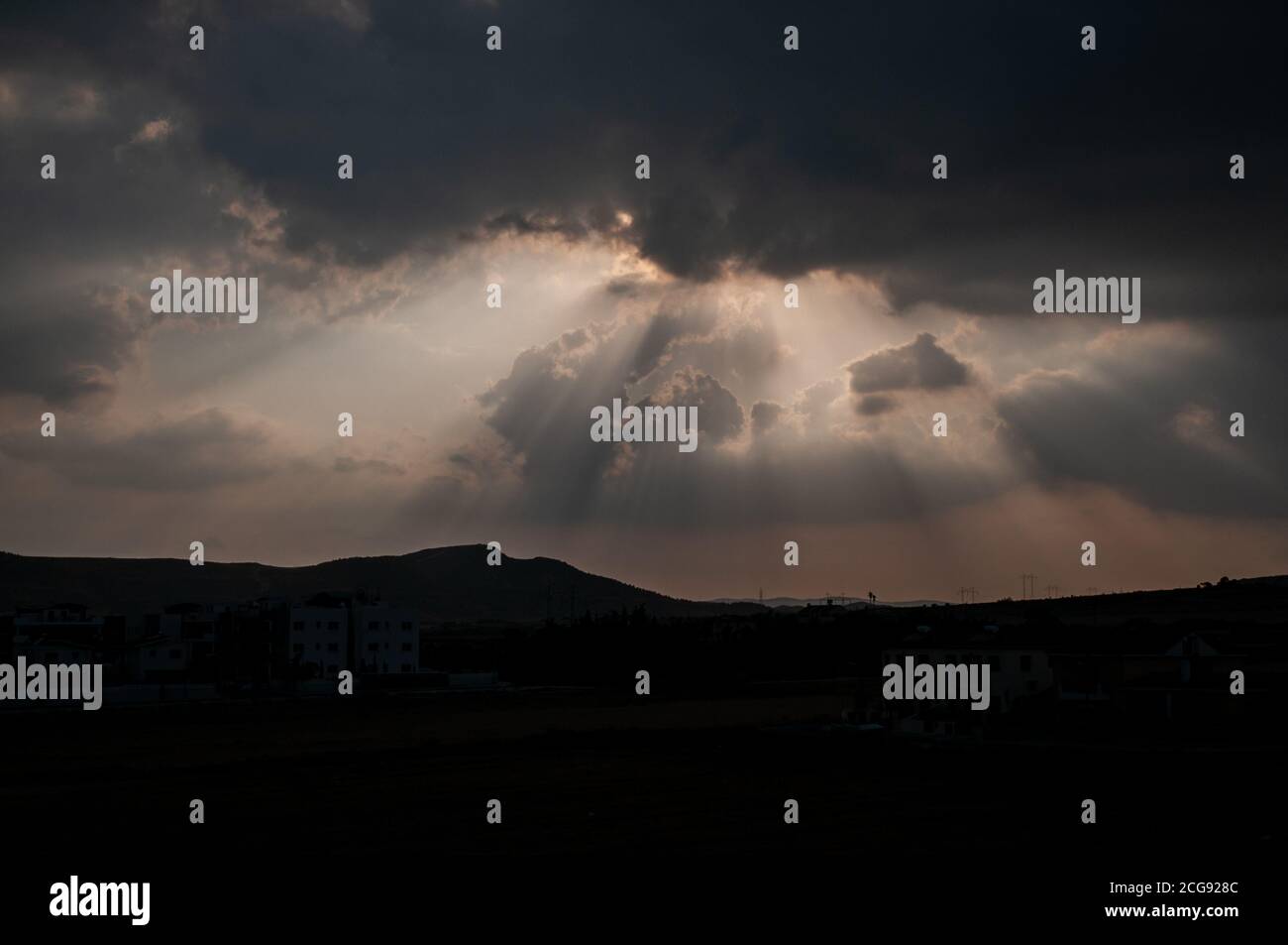 Raggi di luce solare che si infrangono attraverso nuvole pesanti su paesaggi silhouette di Cipro sud-orientale. Foto Stock