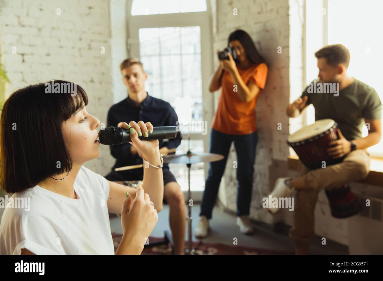 Sessione. Band musicista jamming insieme in un posto di lavoro d'arte con strumenti. Uomini e donne caucasici, musicisti, suonando e cantando insieme. Concetto di musica, hobby, emozioni, occupazione artistica. Foto Stock