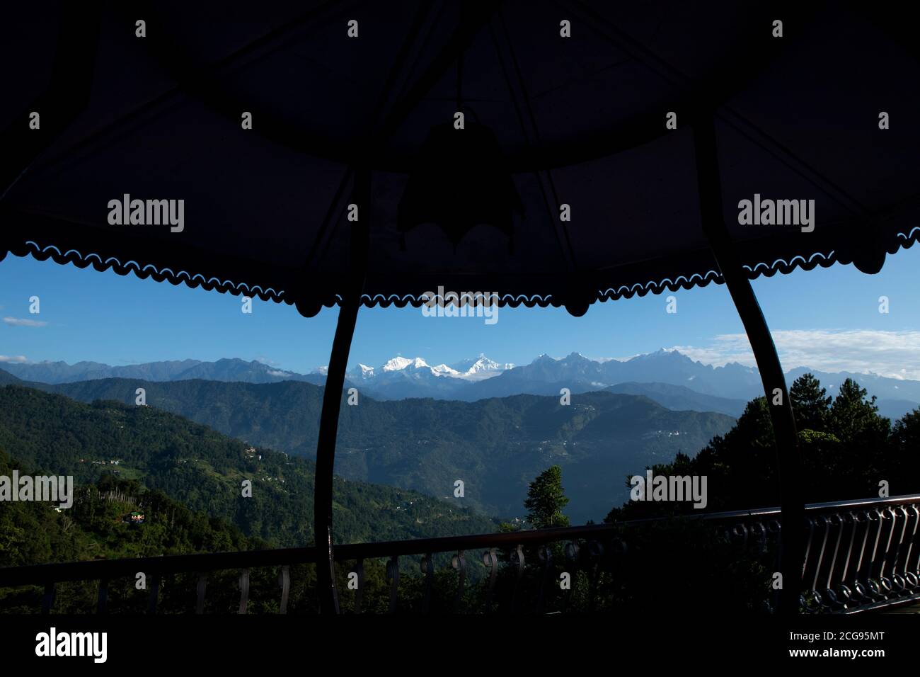 Il possente Kanchanjunga con altre cime innevate sullo sfondo di un piccolo villaggio sul pendio delle montagne sopra L'Himalaya dal balcone di un tou Foto Stock