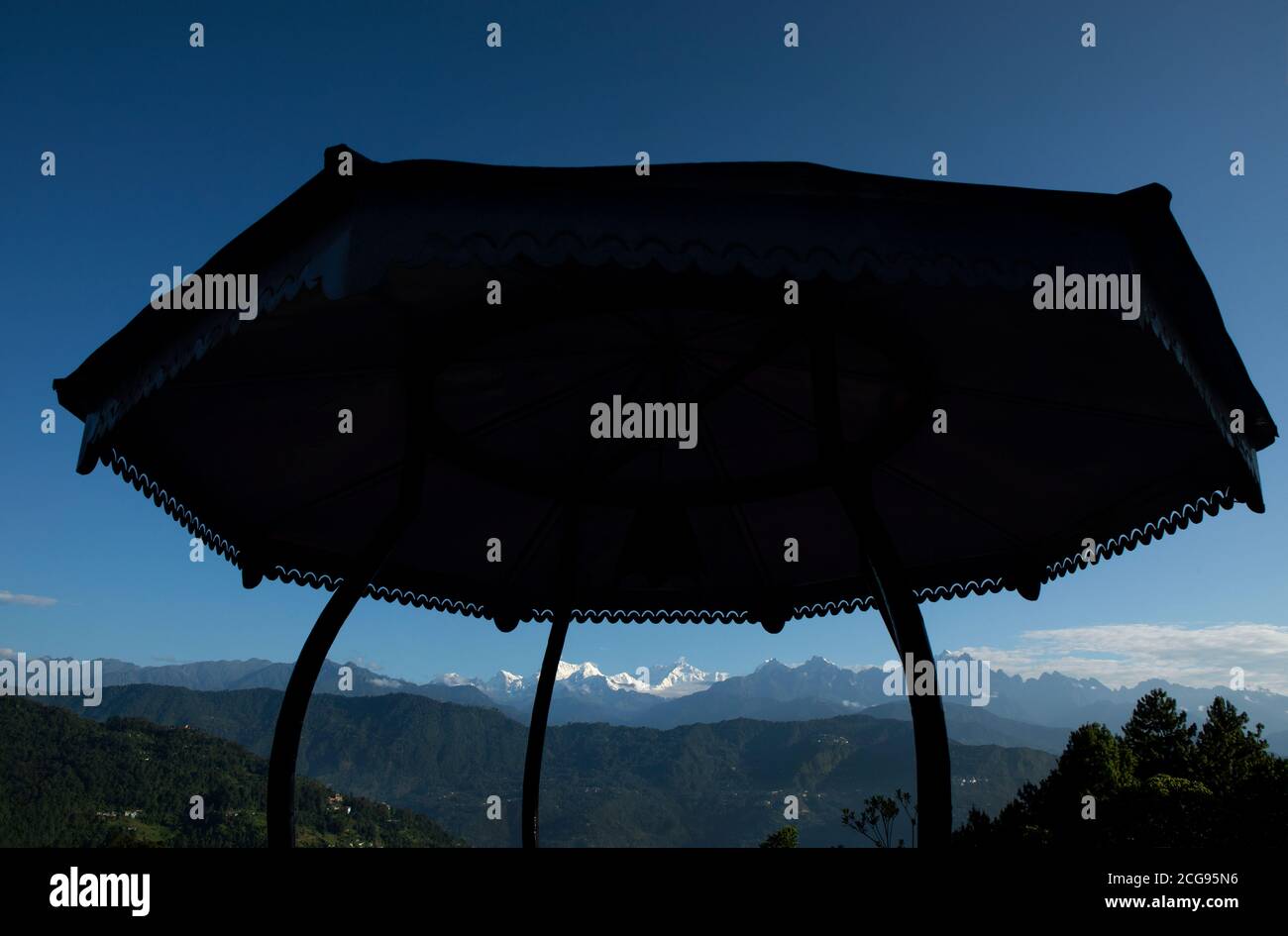 Il possente Kanchanjunga con altre cime innevate sullo sfondo di un piccolo villaggio sul pendio delle montagne sopra L'Himalaya dal balcone di un tou Foto Stock