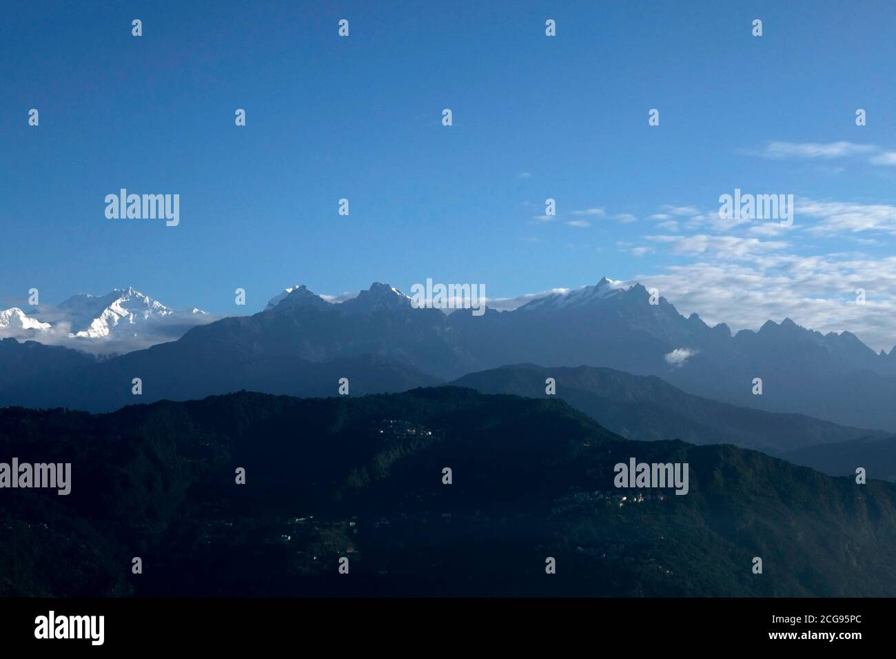 Il possente Kanchanjunga con altre cime innevate sullo sfondo di un piccolo villaggio sul pendio delle montagne sopra L'Himalaya a Sikkim Foto Stock