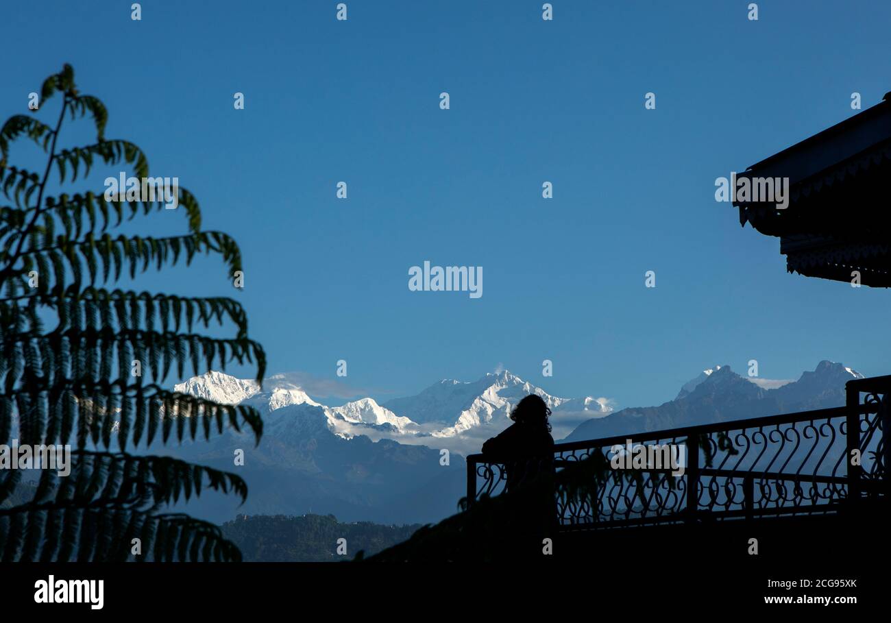 Il possente Kanchanjunga con altre cime innevate sullo sfondo di un piccolo villaggio sul pendio delle montagne sopra L'Himalaya dal balcone di un tou Foto Stock