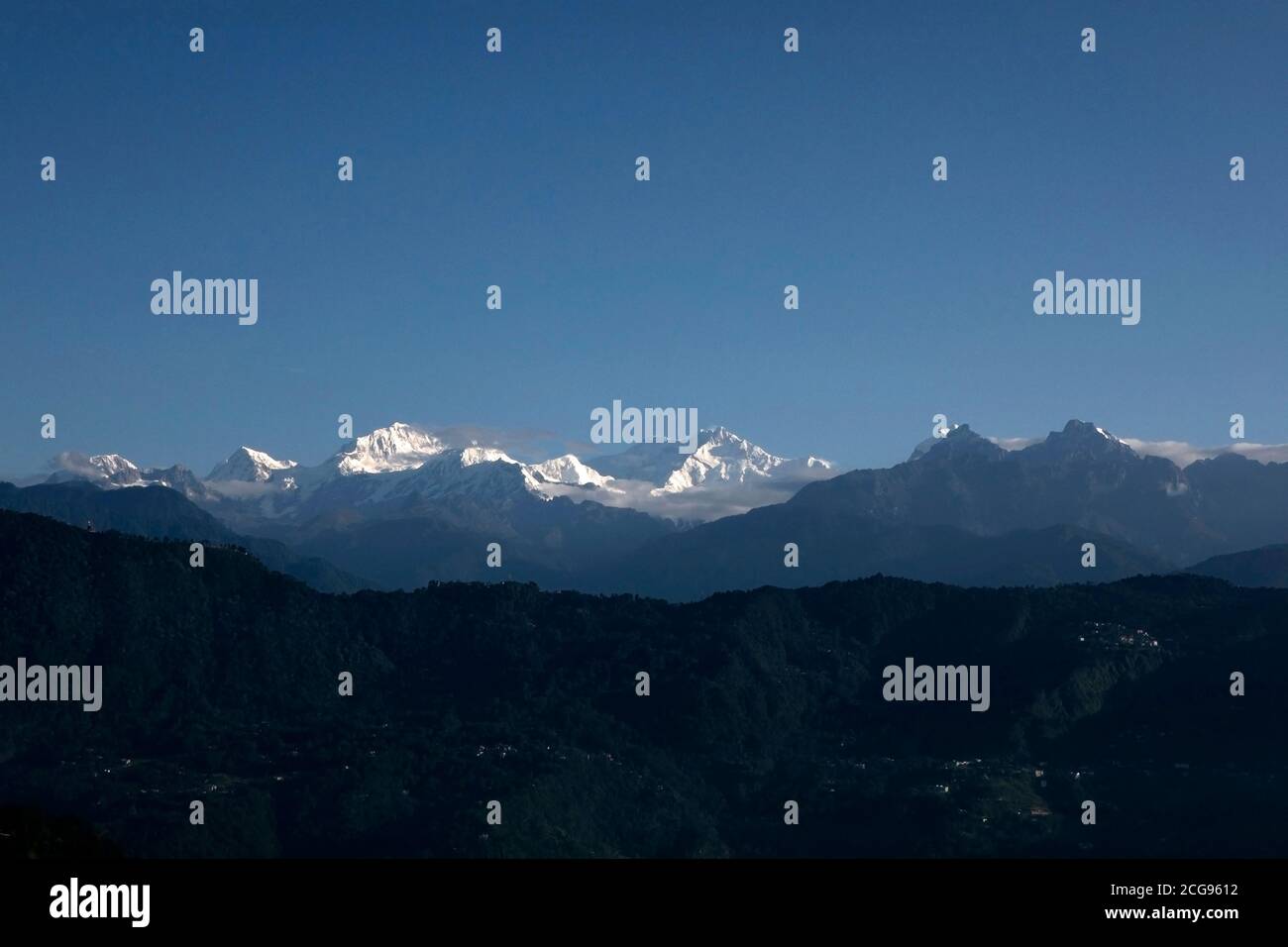 Il possente Kanchanjunga con altre cime innevate sullo sfondo di un piccolo villaggio sul pendio delle montagne sopra L'Himalaya a Sikkim Foto Stock