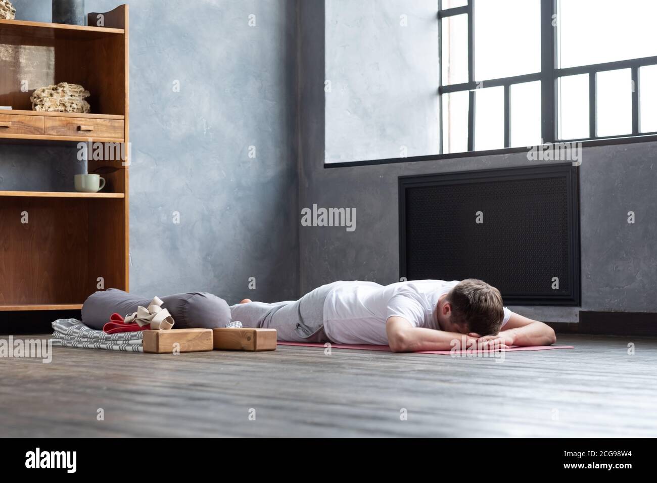 Uomo che riposa dopo la pratica di yoga sul pavimento in makarasana. Foto Stock