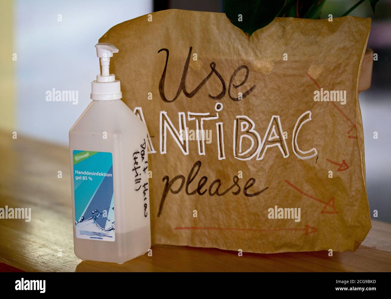 Una borsa marrone si trova su uno scaffale in un bar con un testo scritto a mano che dice "Usa l'antibac, per favore." Accanto ad esso si trova una disinfezione bottiglia. Foto Stock