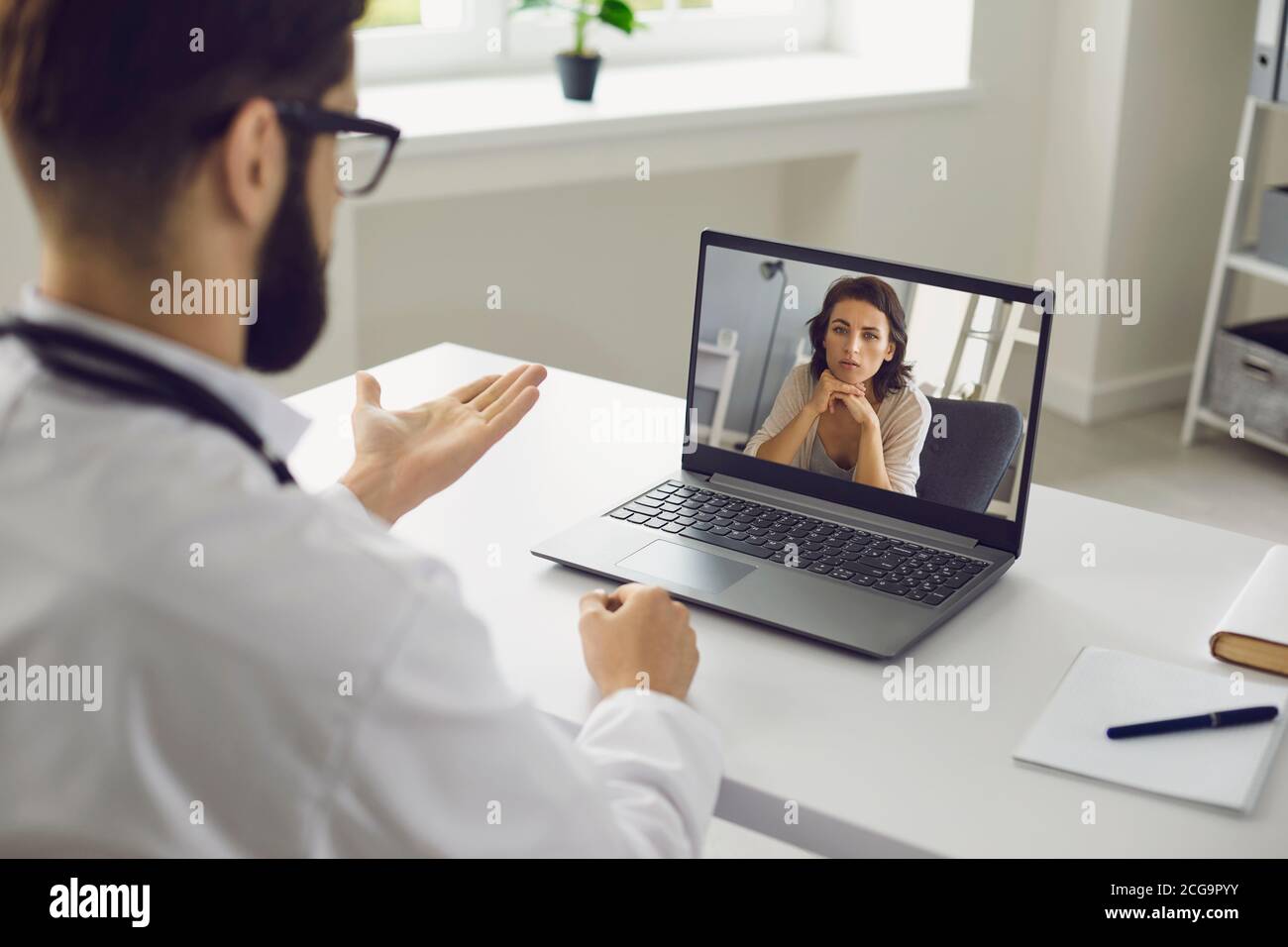Consultazione medica online. Un uomo seduto nel suo ufficio usa un laptop, una videochiamata e ascolta un paziente. Foto Stock