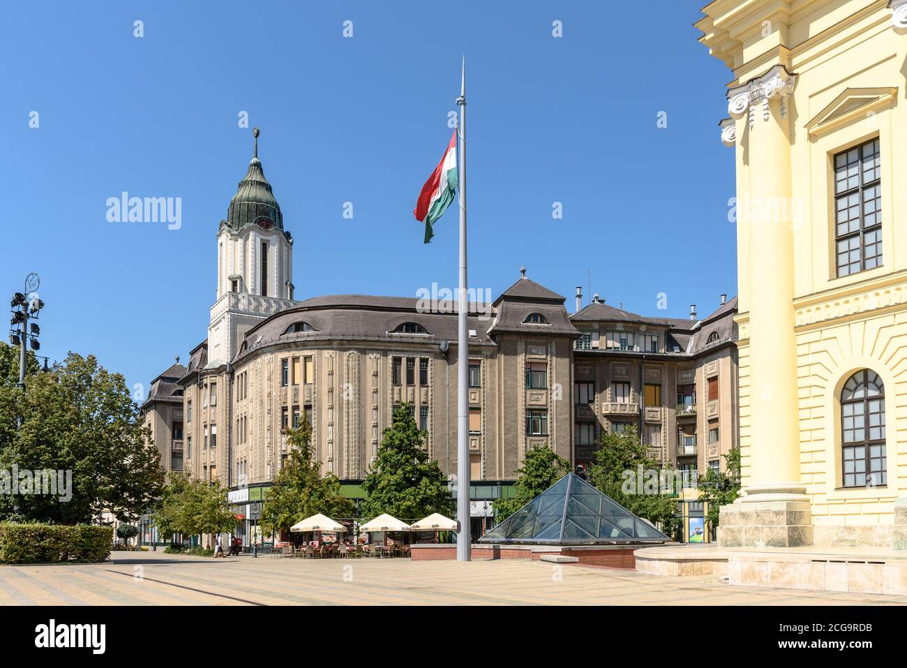 Un flagpole con il tricolore ungherese davanti ad un Edificio in stile Art Nouveau accanto alla chiesa nel centro di Debrecen Foto Stock