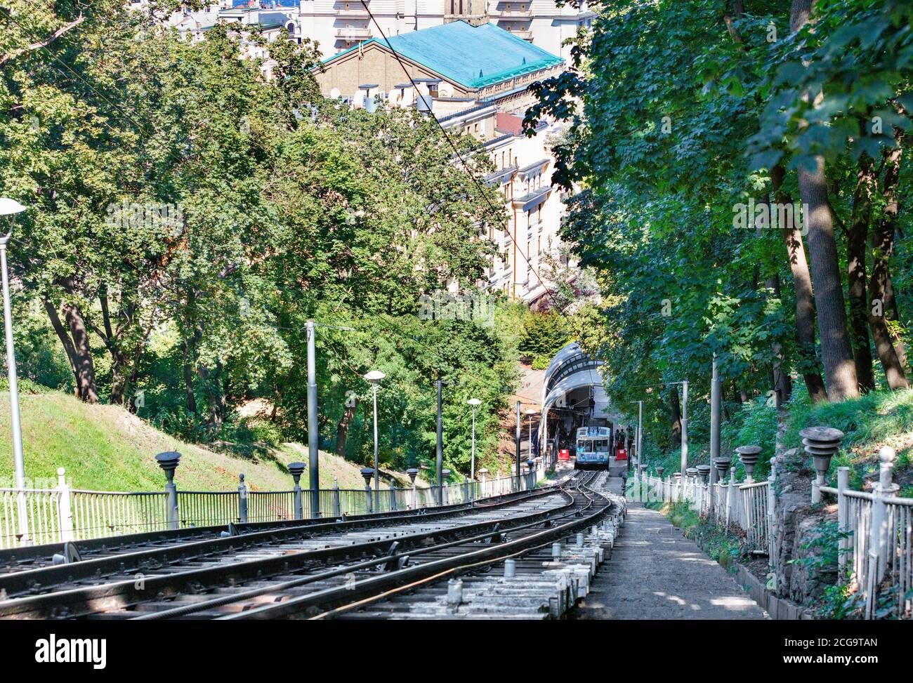 Una funicolare a fune, circondata dal verde fogliame di un parco estivo, raccoglie i passeggeri alla stazione inferiore per sollevarli sul versante montano. Foto Stock