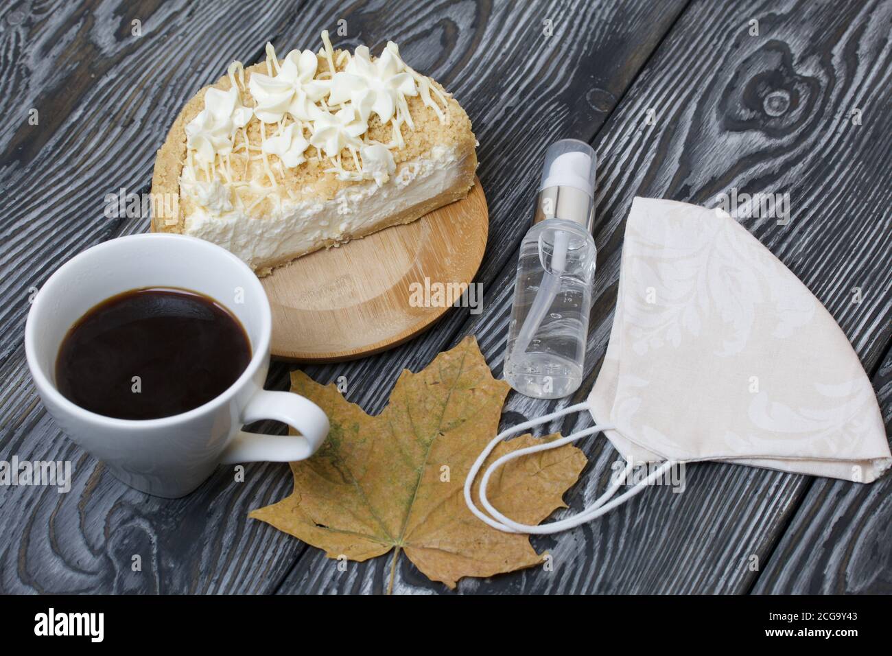 Cheesecake con cioccolato bianco e una tazza di caffè. Il ripieno è visibile sul taglio del dessert. Nelle vicinanze si trova una maschera medica, antisettica e secca Foto Stock