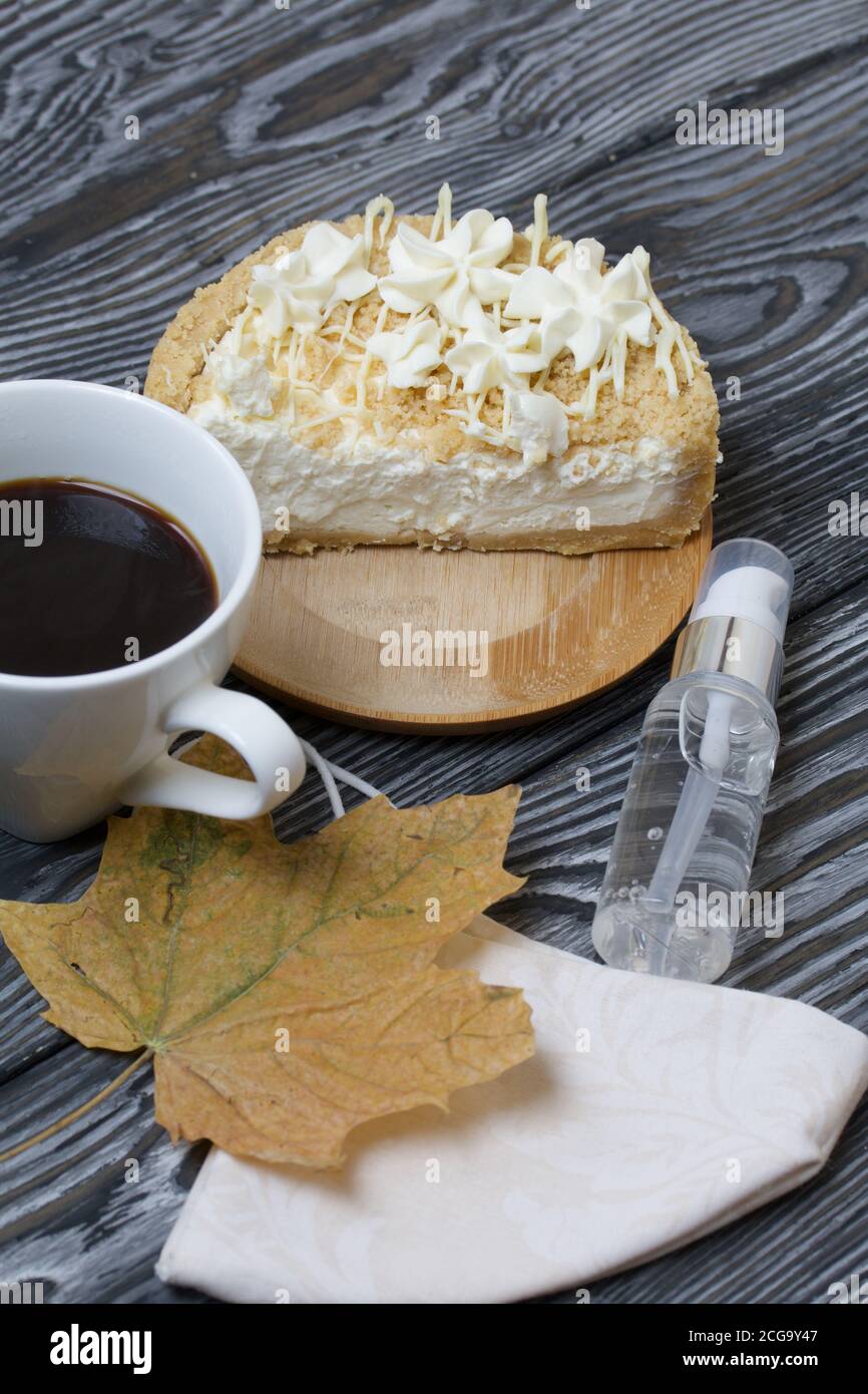 Cheesecake con cioccolato bianco e una tazza di caffè. Il ripieno è visibile sul taglio del dessert. Nelle vicinanze si trova una maschera medica, antisettica e secca Foto Stock