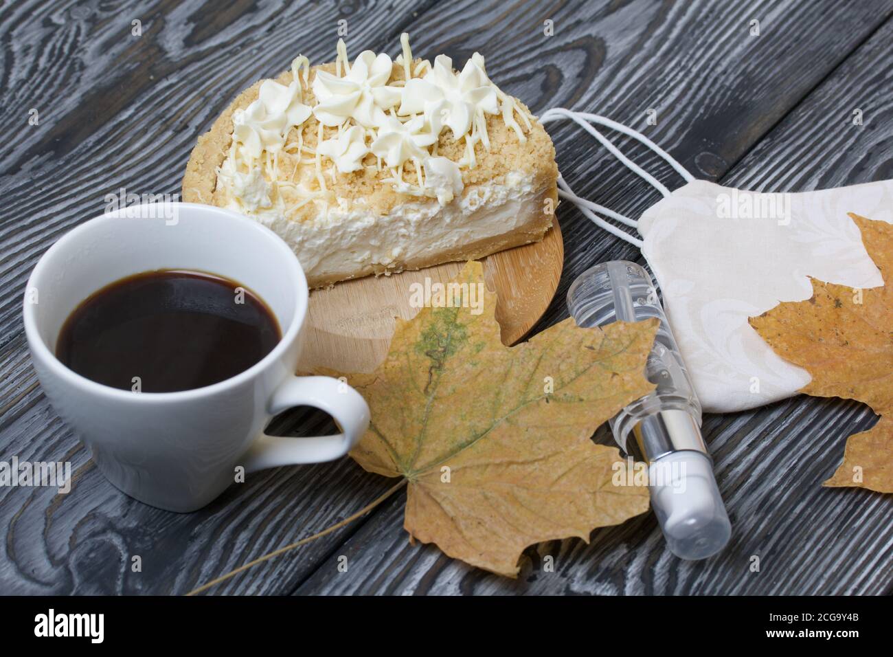 Cheesecake con cioccolato bianco e una tazza di caffè. Il ripieno è visibile sul taglio del dessert. Nelle vicinanze si trova una maschera medica, antisettica e secca Foto Stock