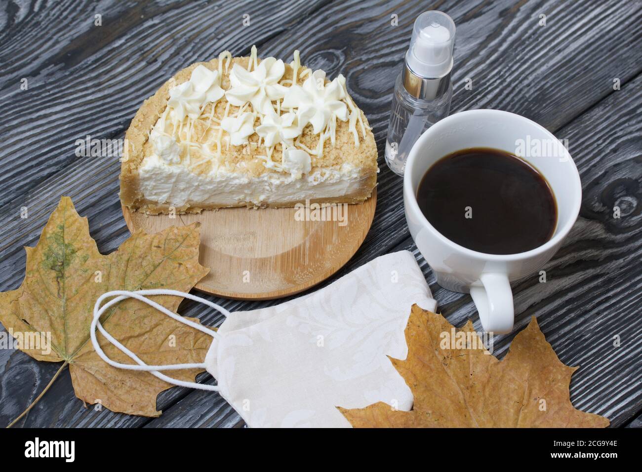 Cheesecake con cioccolato bianco e una tazza di caffè. Il ripieno è visibile sul taglio del dessert. Nelle vicinanze si trova una maschera medica, antisettica e secca Foto Stock