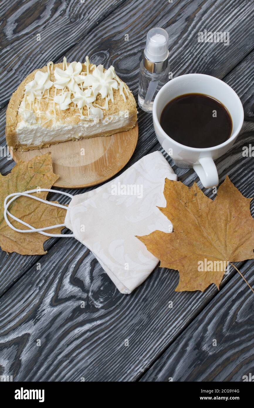Cheesecake con cioccolato bianco e una tazza di caffè. Il ripieno è visibile sul taglio del dessert. Nelle vicinanze si trova una maschera medica, antisettica e secca Foto Stock