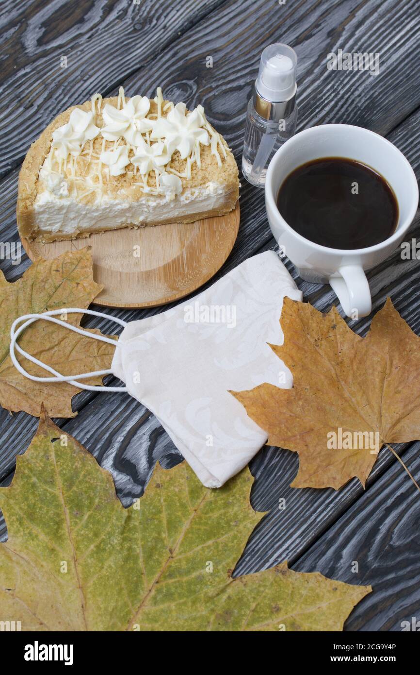 Cheesecake con cioccolato bianco e una tazza di caffè. Il ripieno è visibile sul taglio del dessert. Nelle vicinanze si trova una maschera medica, antisettica e secca Foto Stock