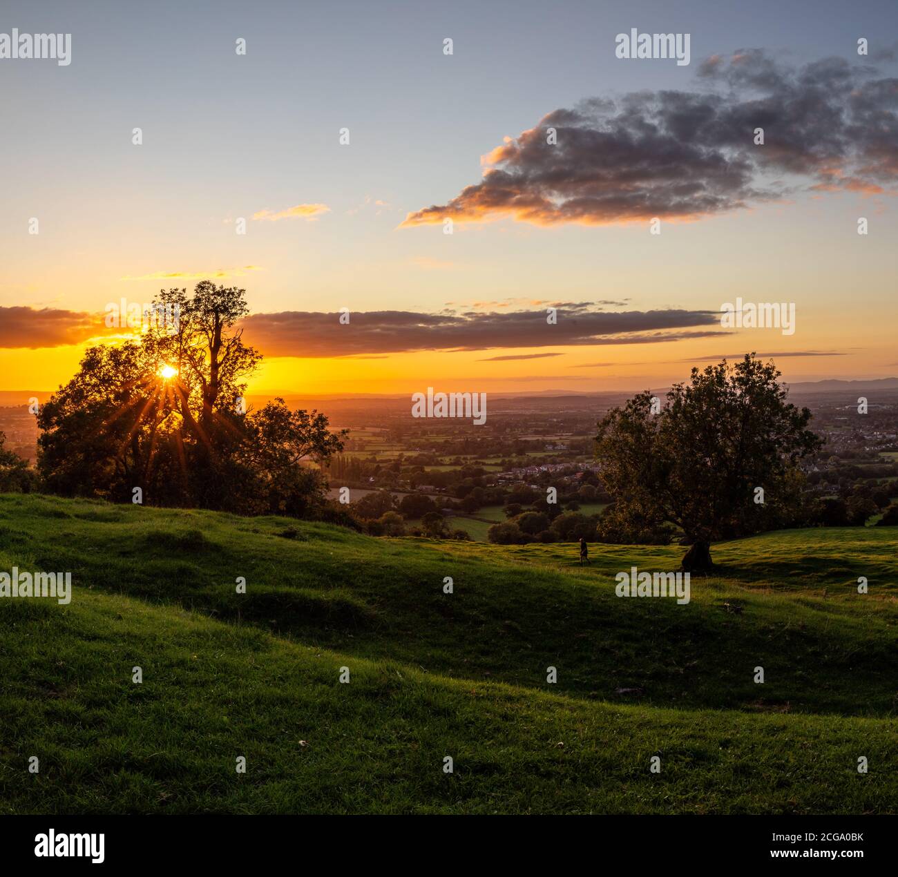 Il sole impostazione. Vista da Lechampton Hill sulla strada che va nella città termale locale nel Cotswolds chiamato Cheltenham in Gloucestershire Inghilterra. Foto Stock