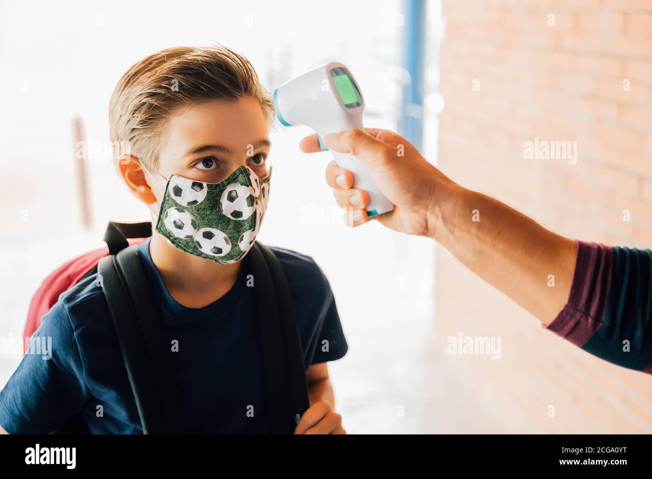 insegnante che prende la temperatura di un ragazzo con un termometro durante la pandemia di covid. Foto Stock