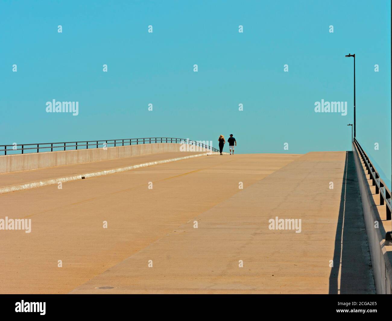 Coppia che cammina sul ponte da solo con lontano cielo blu davanti. Contrasto tra terra e cielo, passato e futuro. Spazio di testo disponibile. Foto Stock