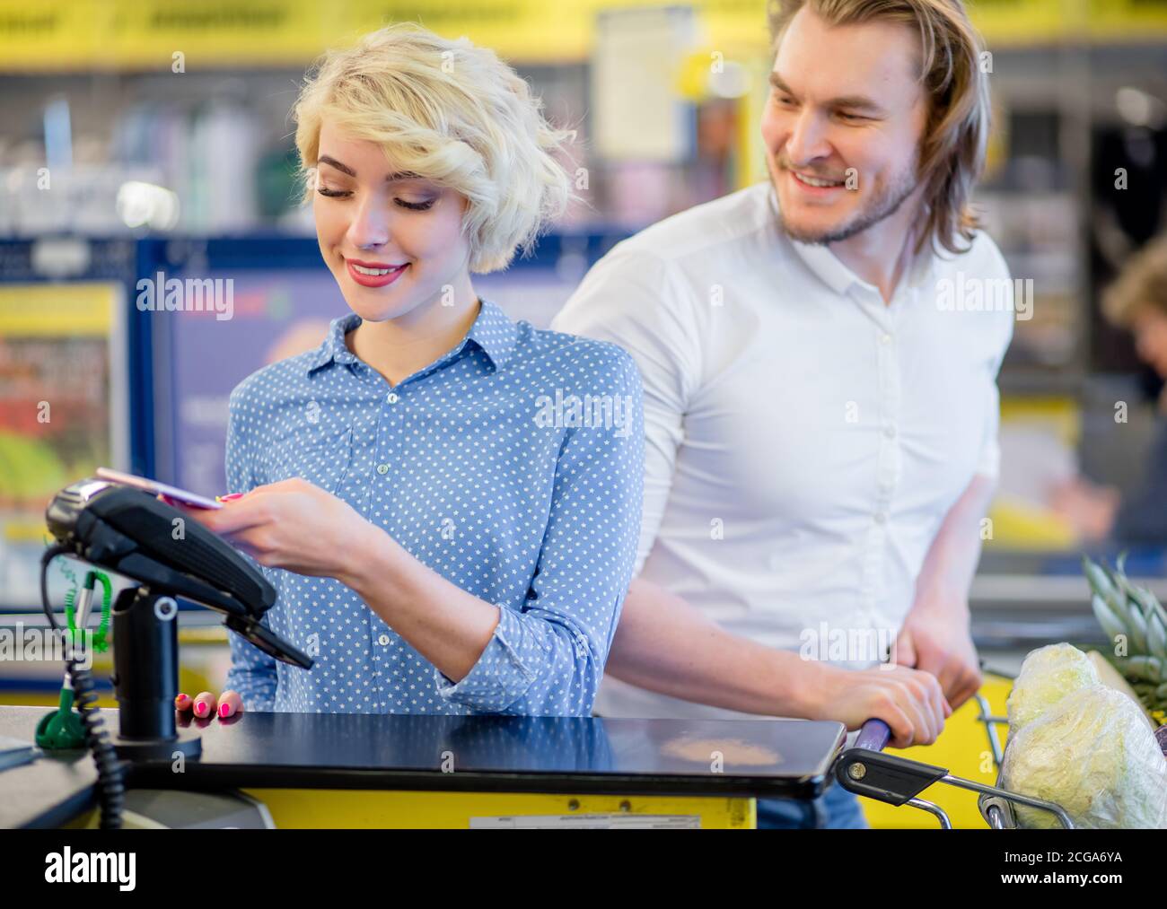 Bionda attraente donna al checkout supermercato, sta pagando usando una carta di credito, shopping e concetto di vendita al dettaglio. Foto Stock