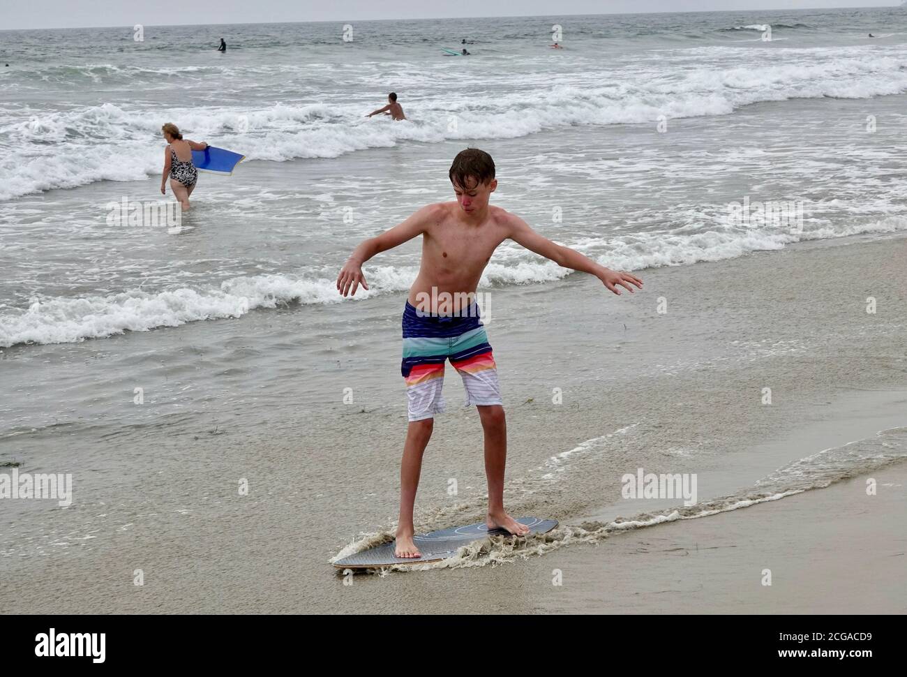 Un ragazzo adolescente va a skim boarding sulle onde più vicine al litorale della spiaggia. Foto Stock