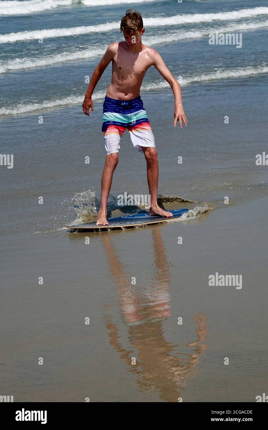 Un ragazzo adolescente va a skim boarding sulle onde più vicine al litorale della spiaggia. Foto Stock