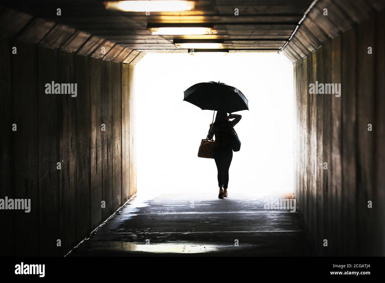 Silhouette altamente saturata di una donna sicura che tiene un ombrello che esce da un tunnel. Tempo libero lavoro città chic stile di vita. Previsioni del tempo, pioggia Foto Stock