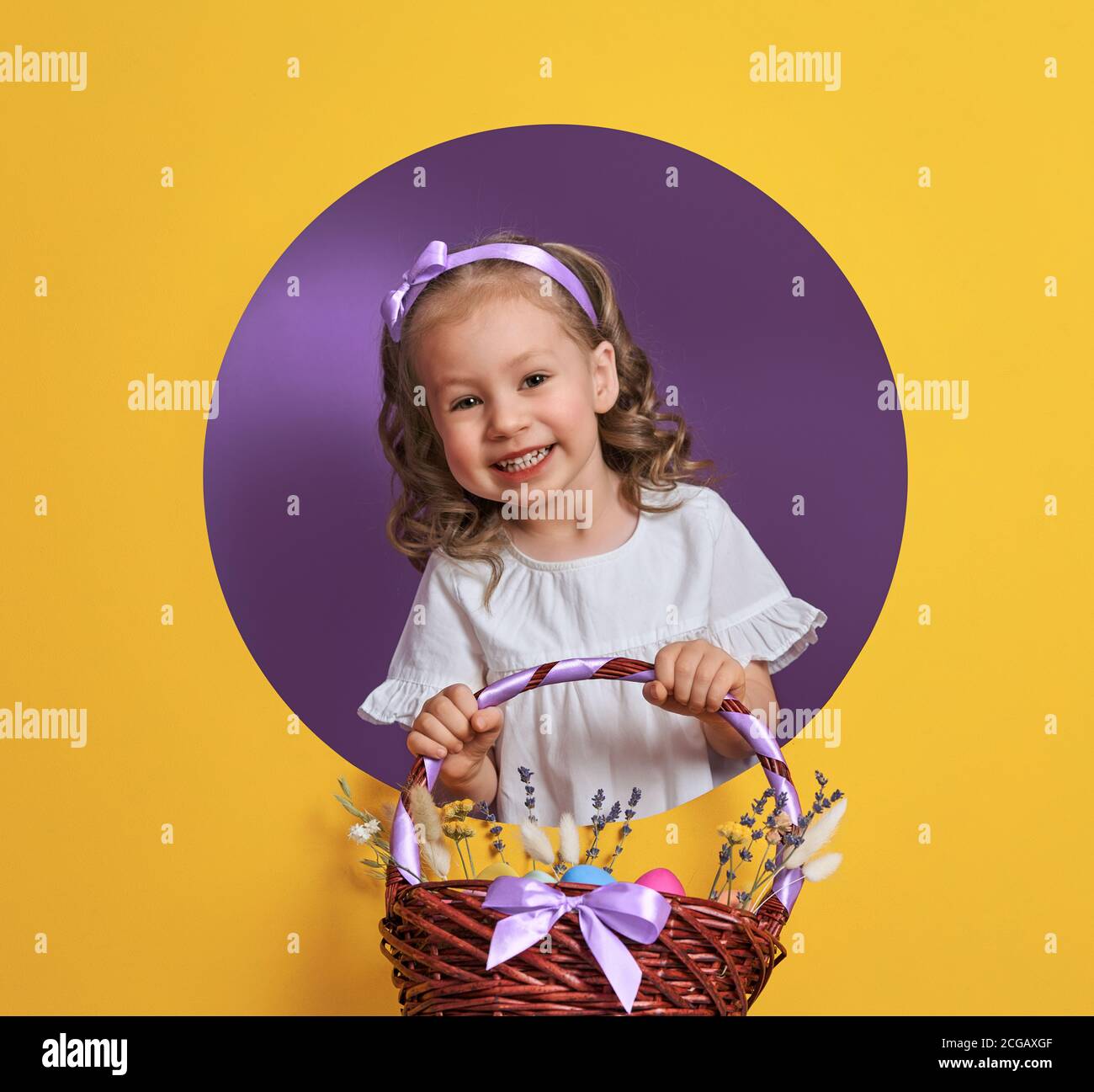 Carino bambino piccolo il giorno di Pasqua. Ragazza con uova dipinte su sfondo viola chiaro e giallo. Foto Stock