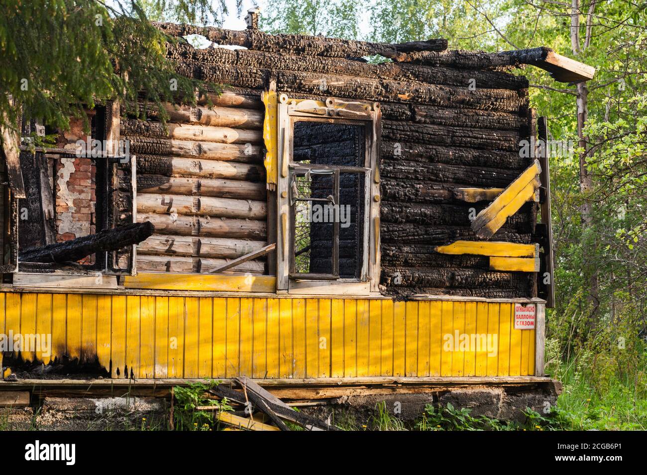 Muro di casa rurale giallo bruciato con finestre vuote e cartello di avvertimento. Testo in russo significa: Infiammabile, bombole di gas Foto Stock