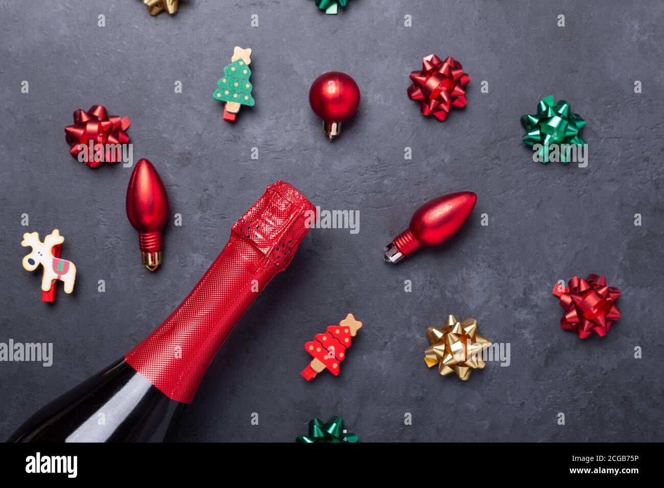 Composizione natalizia con champagne e regali rossi, verdi, dorati e archi su sfondo di pietra scuro. Concetto di Natale e Capodanno - immagine Foto Stock