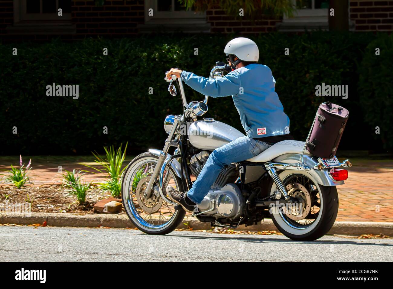 Chestertown, MD, USA 08/30/2020: Un uomo che indossa casco, jeans e un cappotto casual sta cavalcando una moto d'epoca in città. Ha una borsa a sella marrone wh Foto Stock