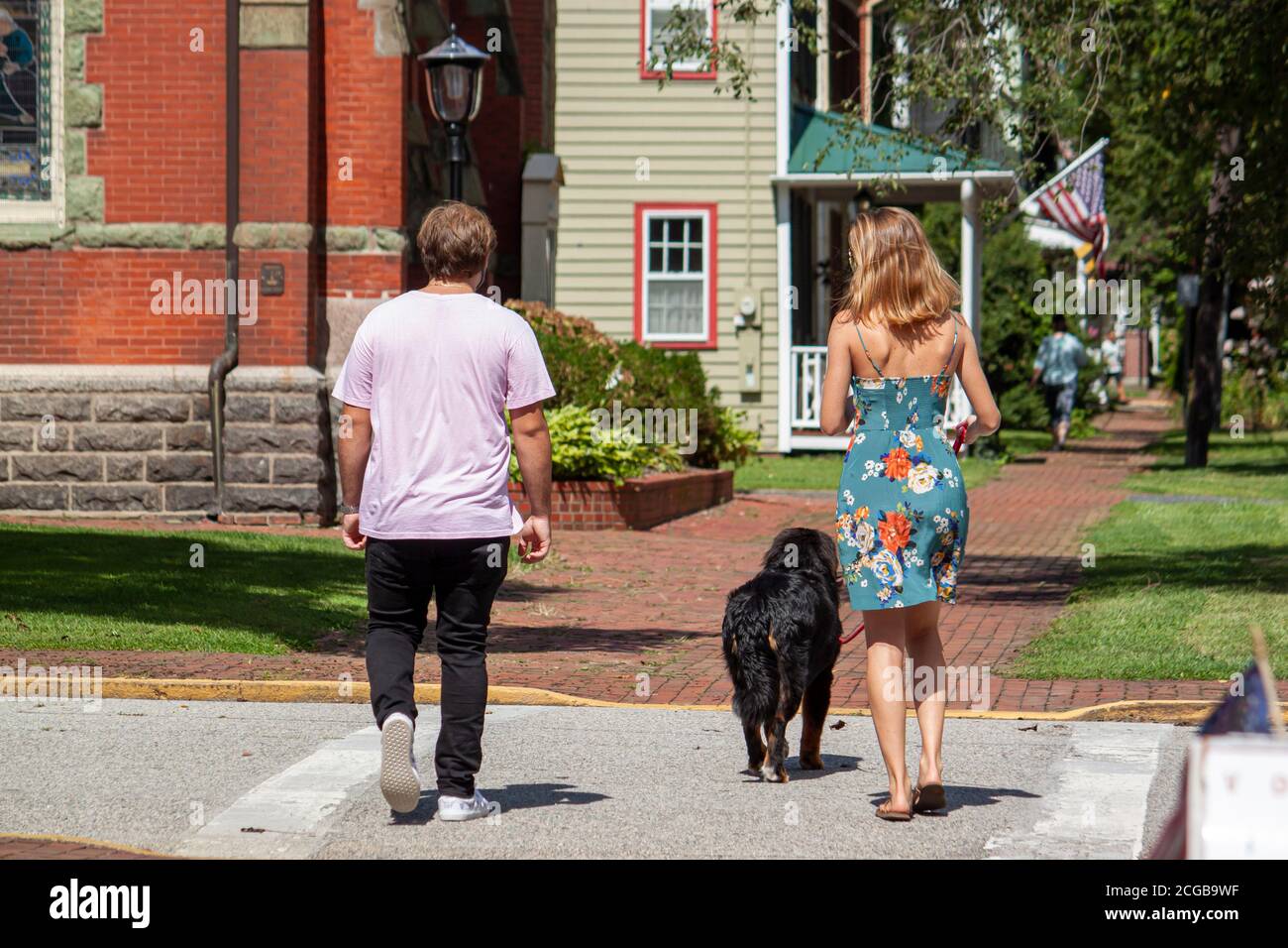 Una giovane coppia caucasica cammina nel quartiere storico di Chestertown, nel Maryland con il loro cane. La donna ha un colore chiaro dei capelli e indossa un colore floreale Foto Stock